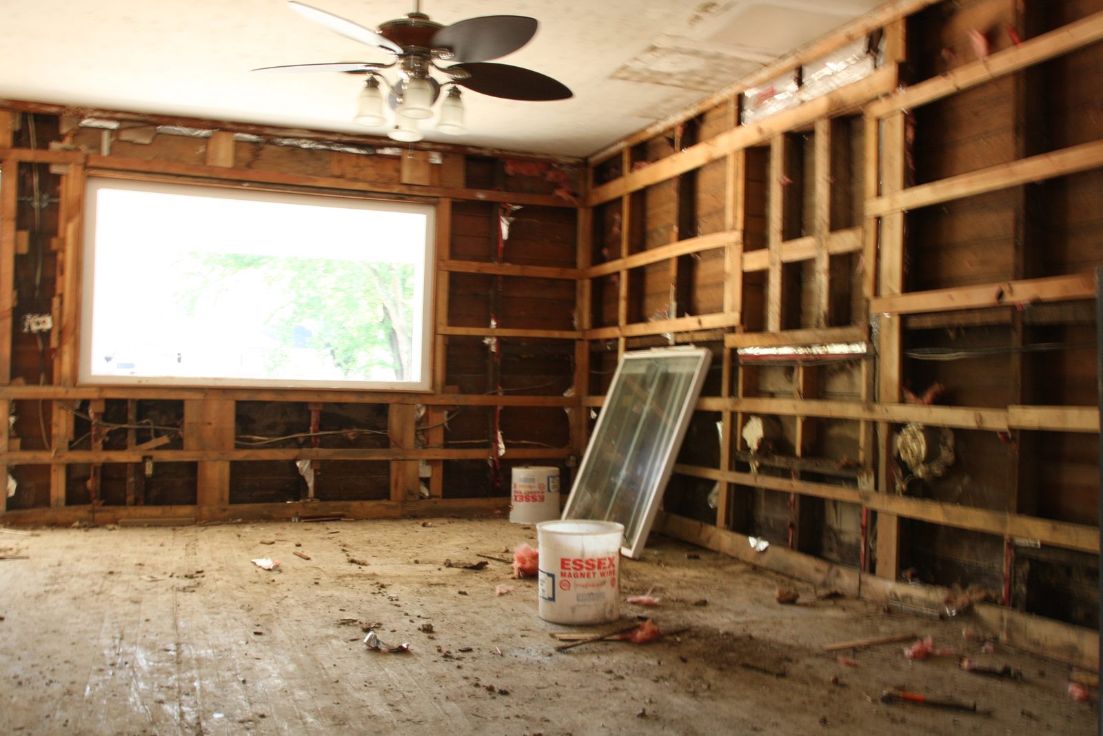 Living room opened to the studs after a flood, wet drywall and insulation removed, ceiling fan still in place